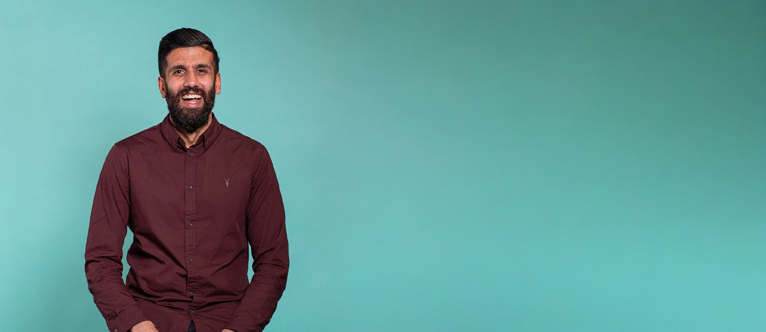 Zubair Mohammad, fractional CMO & founder of a marketing agency, stands smiling in front of a teal background